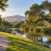 A paved path winding beside a calm canal with green grass and oak trees at Heather Farm Park.