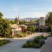 A civic campus with a clock tower, palm trees, and U.S. and California flags under a blue sky.