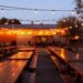 String lights over picnic tables in an outdoor beer garden at dusk