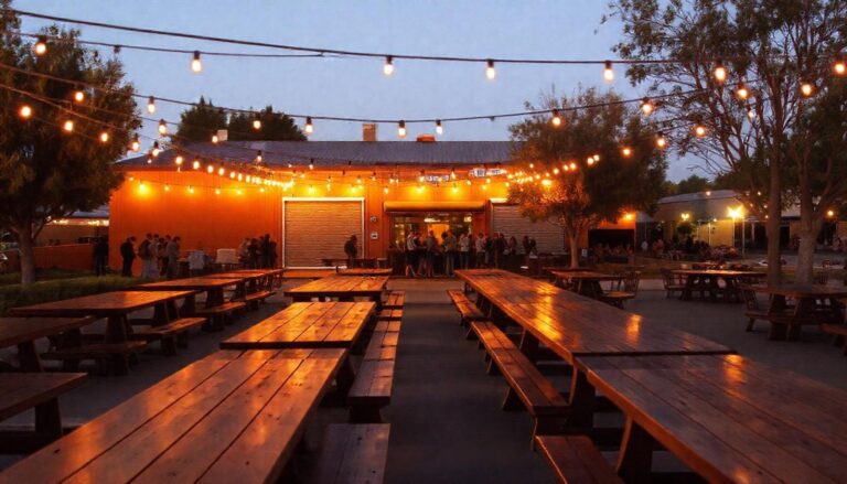 String lights over picnic tables in an outdoor beer garden at dusk